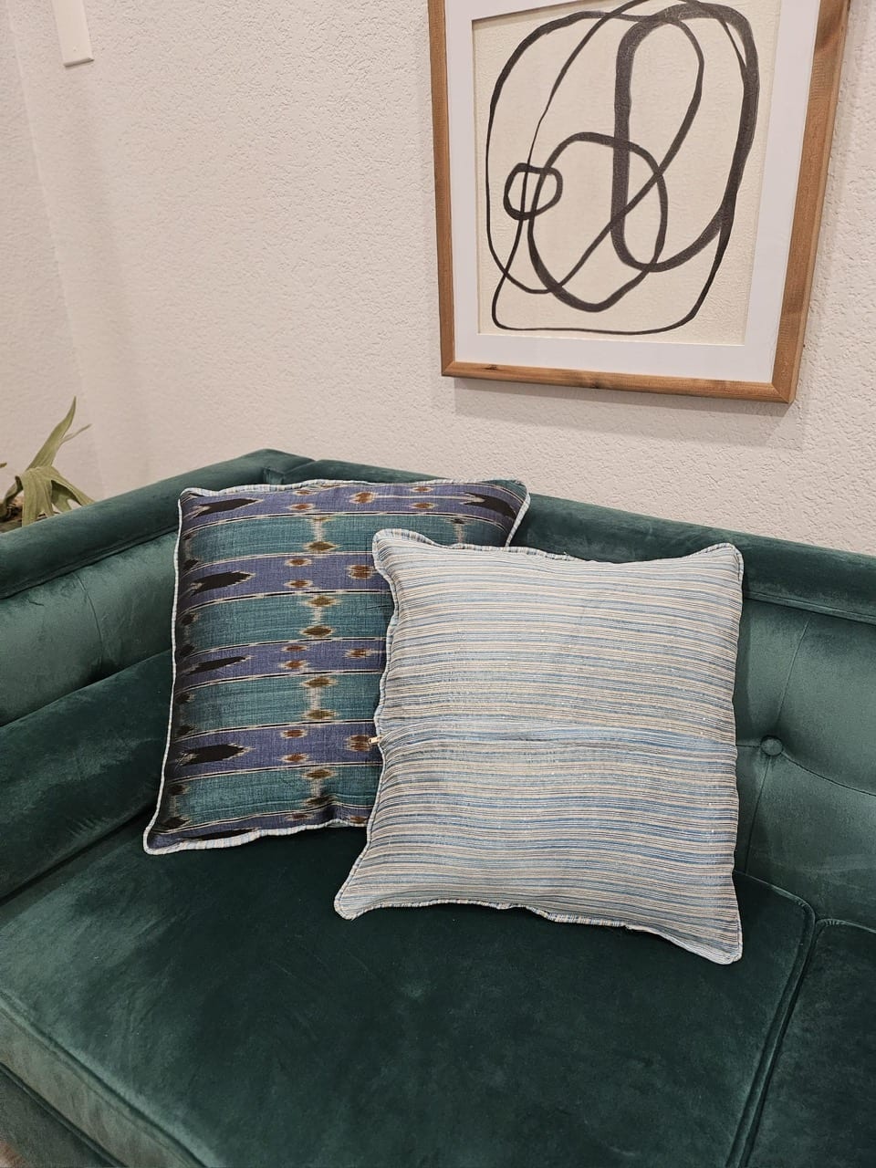 Two handmade cushion covers (one in purple and teal ikat, one in blue stripe) on a velvet sofa